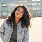 Happy young woman wearing denim jacket laughing on street.