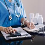 Hand of a health care worker using a calculator and notepad.