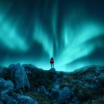 Aurora borealis and young woman on mountain peak at night.