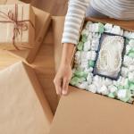 Person opening a shipment of jewelry, with a pearl necklace in a box filled with packing peanuts.