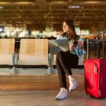 Female passenger on phone and laptop sitting in terminal waiting for her flight.