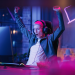 A person cheering at a computer in a dim room with neon lights.