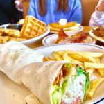 A table at IHOP with plates of brunch items, including a chicken and bacon wrap with fries, chicken and waffles, bacon, and a stack of pancakes.