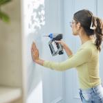 A young woman drilling a hole in her home wall.