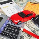 Red toy car surrounded by four calculators and a red pencil sitting on top of U.S. currency to represent the fees required when purchasing a car.