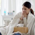 Young woman with a cold sitting under a blanket on a sofa.
