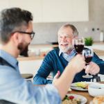 An adult son and his senior father toasting with wine during a light lunch.