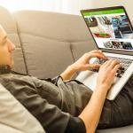 Man lying on sofa while using his laptop to browse for cars online.