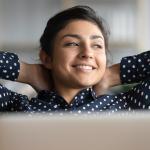 Satisfied woman happily sitting  at work with her hands behind her head.
