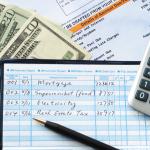 Balancing a checkbook with U.S. bills and calculator and bills visible on a table.