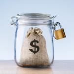 Concept of an emergency fund - a mini bag with a dollar symbol on it locked inside a jar.