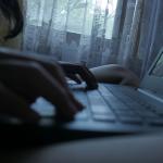 Silhouette of a person typing on a laptop at home.