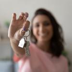 A young female homeowner holding up the keys to her house.