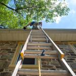 Low angle view of a man on a ladder cleaning a home's gutters.