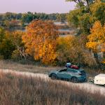 A blue 2020 Honda CR-V towing a 1990 Coleman Columbia pop-up camper on the road towards Antelope Lake in Kansas during autumn.