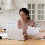 Young female at home using a laptop and reading financial documents.