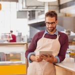 A coffee shop owner using a tablet inside the shop's kitchen.