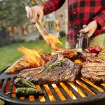Assorted meat like sausages and steak with vegetables being grilled on a BBQ grill outdoors.