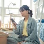 A college student using her smartphone in her dorm while unpacking personal items.