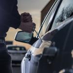 A thief trying to break into a car window with a screwdriver.