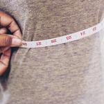 A tailor taking measurements of a client's torso with a tape measure.