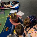 A group of young children during nap time at TLC for Tots daycare center in Nampa, Idaho. One child is sleeping while others are playing.