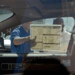 Interior view of car from driver's side looking out passenger window where two people are reading a sticker on the window with the car's features. 