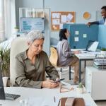 A senior businesswoman working at her desk in an open office setting.