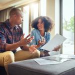 A young couple discussing finances while holding paperwork.