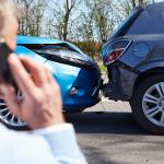 A car driver talks on the phone while looking at a rear-end collision.