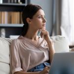 A young woman at home contemplating on couch while using laptop.
