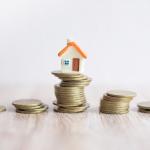 A miniature house on top of a stack of coins.