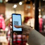 A person scans a QR code in a smartphone in front of a clothing store.