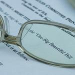 A pair of eyeglasses magnified on the words 'One Big Beautiful Bill' (Act) on a document.