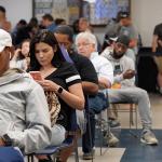 People seated for a queue where most are waiting by being on their phones.