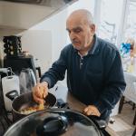 A senior man cooking a dish in his brightly-lit kitchen at home.