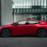 A red 2024 Toyota Prius Prime parked in front of a building on a city street.