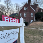 A sign in foreground lists a home for rent in Maryland with tall brick home in the background. Municipal rental registries are gaining attention as cities try to get a handle on who owns rental properties and where, both to better understand their housing landscape and to ensure rentals are safe for tenants. 