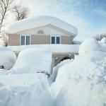 A house and its cars covered in deep white snow after a blizzard.
