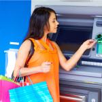 A young woman at the ATM carrying colored shopping bags 