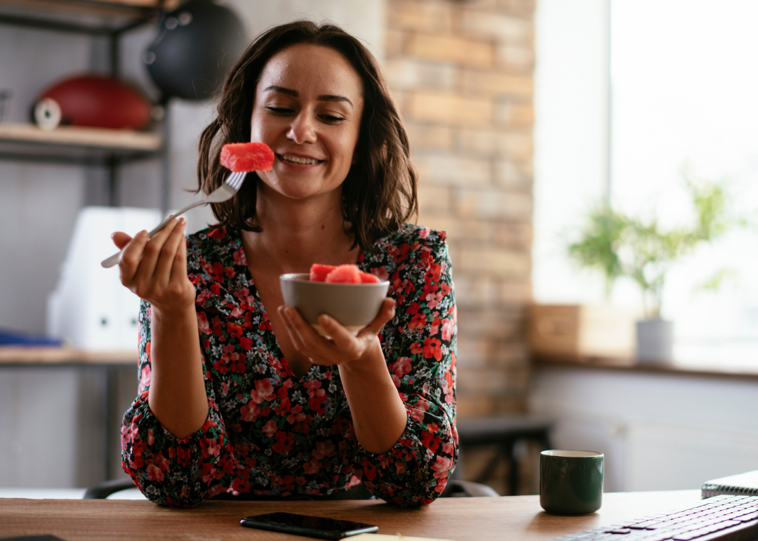 Woman eating fruit at desk.