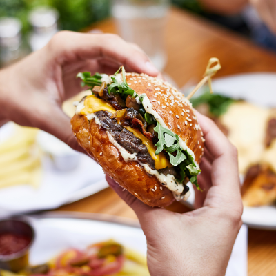 Close up hands holding burger at outdoor restaurant table.