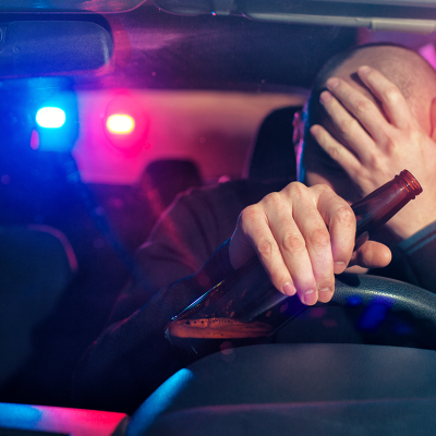 Driver with bottle in hand with police lights behind them.