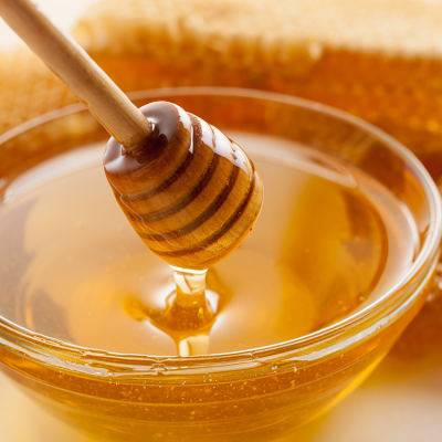 Closeup honey dripper, glass bowl of honey, and honeycomb.