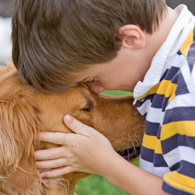 Five-year-old boy puts his forehead on a dog's head, holding the dog's face in his hands. 
