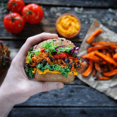 A plant-based sandwich is held in front of a backdrop of other plant foods.