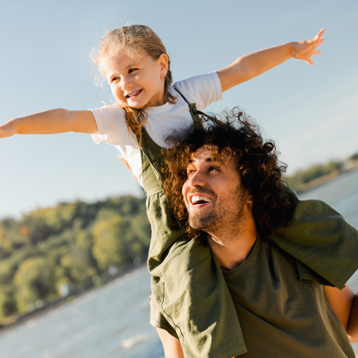 Father with daughter on shoulders walking at beach.