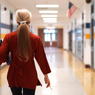 Rear view of teacher walking down school hallway.