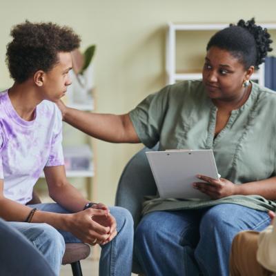 Psychologist talking to teenage boy during therapy session.