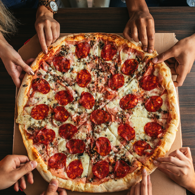Group of people’s hands grabbing a slice of pizza.